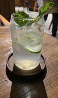 Selective focus, Delicious refreshing summer mojito with ice, lime and mint in a glass with grops. wood background photo