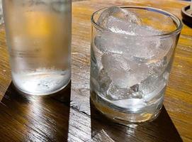 Selective focus, A clear glass filled with ice and clear glass bottle holds cold mineral water sits on wooden table photo