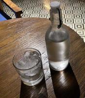 Selective focus, A clear glass filled with ice and clear glass bottle holds cold mineral water sits on wooden table photo