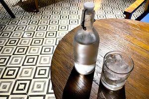 enfoque selectivo, un vaso transparente lleno de hielo y una botella de vidrio transparente contiene agua mineral fría sobre una mesa de madera foto