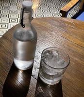 Selective focus, A clear glass filled with ice and clear glass bottle holds cold mineral water sits on wooden table photo