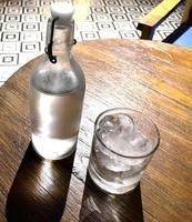 enfoque selectivo, un vaso transparente lleno de hielo y una botella de vidrio transparente contiene agua mineral fría sobre una mesa de madera foto