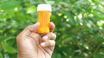 Die linke Hand eines Erwachsenen hält und dreht eine orangefarbene Tablettenflasche mit weißen Tabletten im Inneren video