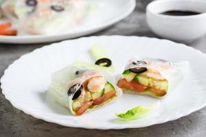 Spring roll cut in half in rice paper with seafood and vegetables on a plate on the table. Close-up photo