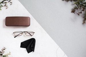 Metal-framed eyeglasses, case and cleaning cloth on a two-tone background. photo