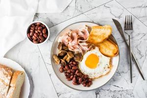 English breakfast with fried egg, bacon, beans, mushrooms and toast on a plate. Top view photo