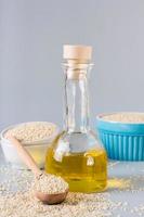 Sesame oil in a bottle and sesame seeds in a bowl on the table. Organic Alternative. Vertical view photo