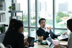 A group of young Asian entrepreneurs. Top Management is meeting to review stock investment data from the team in a meeting room with natural light photo