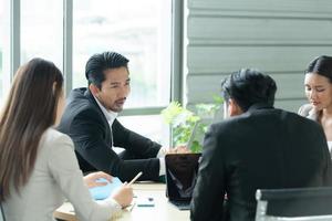 A group of young Asian entrepreneurs. Top Management is meeting to review stock investment data from the team in a meeting room with natural light photo