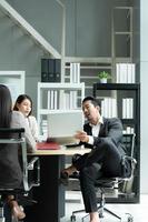 A group of young Asian entrepreneurs. Top Management is meeting to review stock investment data from the team in a meeting room with natural light photo