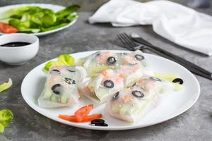 Fresh spring rolls in rice paper made from shrimp, olives and vegetables on a plate on the table. photo