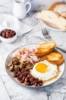 English breakfast with fried egg, bacon, beans, mushrooms and toast on a plate. Vertical view photo