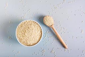 White sesame seeds in a bowl and in a wooden spoon on a gray background. Organic diet. Top view photo