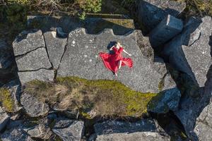 vista aérea de una chica con vestido rojo sobre roca o estructura en ruinas de hormigón foto