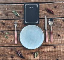 hora de la cena. toma en ángulo alto de plato vacío, tenedor, cuchara, cuchillo y menú cerrado sobre una mesa rústica foto