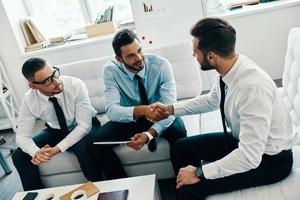 Welcome to our team Young modern men in formalwear shaking hands while working in the office photo