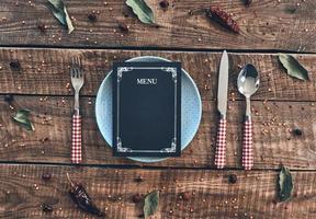 Seat is reserved. High angle shot of empty plate, fork, spoon, knife and closed menu lying on rustic table photo