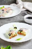 Spring roll cut in half in rice paper with seafood and vegetables on a plate. Vertical view photo