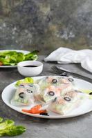 Spring rolls in rice paper made from shrimp, olives, lettuce and vegetables on a plate. Vertical photo