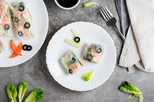 Spring roll cut in half in rice paper with seafood and vegetables on a plate. Top view photo