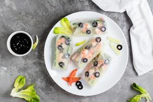 Fresh spring rolls in rice paper made from shrimp, olives and vegetables on a plate. Top view photo