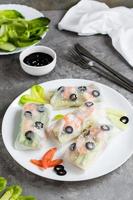 Fresh spring rolls in rice paper made from shrimp, olives and vegetables on a plate. Vertical view photo