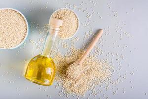 Sesame oil in a glass and seeds in a bowl on the table. Organic Alternative Food. Top view photo