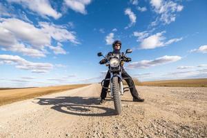man in a black uniform on bike against the backdrop of panorama of field and blue sky. motorcycle travel concept photo