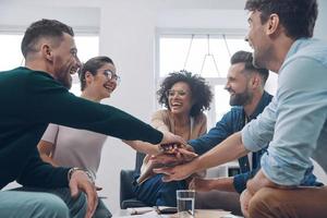 un equipo de negocios joven y confiado que mantiene las manos juntas y sonríe mientras se sientan juntos en la oficina foto