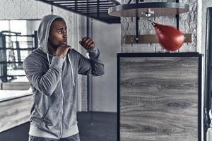 nada más que éxito. apuesto joven africano con ropa deportiva boxeando mientras hace ejercicio en el gimnasio foto