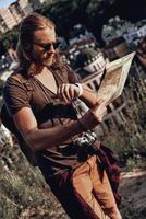 momento. un joven apuesto con ropa informal sosteniendo un mapa y revisando la hora mientras está de pie en la colina al aire libre foto