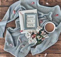 Cozy concept. High angle shot of sweater, flowers, cup of coffee and photo frame on wooden desk