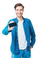 Showing his new smart phone. Cheerful young man stretching out mobile phone and smiling while standing against white background photo