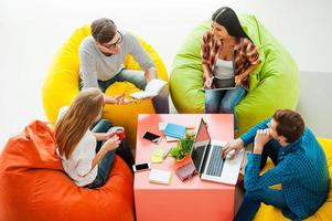 Place where ideas born. Top view of four young people working together while sitting at the colorful bean bags photo