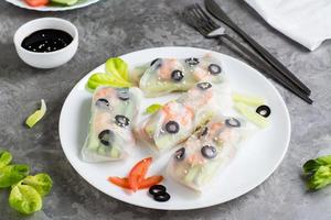 Spring rolls in rice paper made from shrimp, olives, lettuce and vegetables on a plate on the table. photo