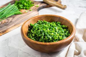 Fresh chopped green onions in a wooden bowl and a cutting board on the table.  Close-up photo