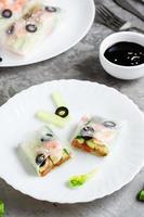 Spring roll cut in half in rice paper with seafood and vegetables on a plate. Close-up vertical photo
