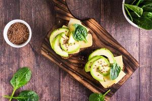 Sandwiches on rye bread with cheese, avocado, spinach and flax seeds on a wooden board. Top view photo