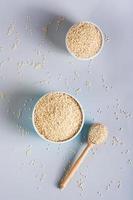 Sesame seeds in bowls and in a wooden spoon on a gray background. Organic food. Top and vertical photo