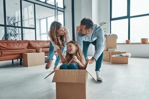 familia joven juguetona sonriendo y desempaquetando sus cosas mientras se muda a un nuevo apartamento foto