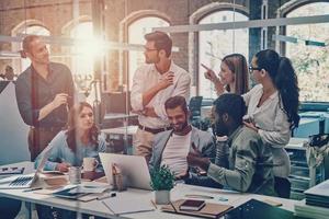 Group of young modern people in smart casual wear communicating and using modern technologies while working in the office photo