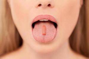 Pill on her tongue. Close-up of young woman holding pill on her tongue photo