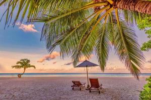 hermoso paisaje tropical de puesta de sol, sillas románticas, tumbonas sombrilla impresionante palmera. arena blanca, horizonte con vista al mar, cielo crepuscular colorido, calma y relajación. increíble complejo de playa para parejas foto