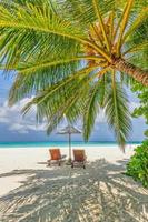 Summer vacation beach, travel scenic. Closeup couple chairs umbrella under palm trees, leaves. Sea sand sky, idyllic recreational landscape. Sunny beautiful tropical island landscape. Amazing paradise photo