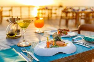 Increíbles mesas románticas para cenar en un restaurante de playa al aire libre. cubierta de madera con velas bajo el cielo del atardecer. vacaciones, amor romántico de luna de miel, cenas de destino de lujo, configuración de mesa exótica con vista al mar foto