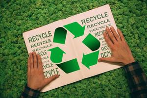 Step to green life. Top view close-up image of man holding hands on his notebook with recycle symbol and text at moss background photo