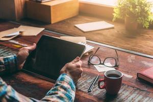 Technologies making life easier. Close-up image of man holding digital tablet with copy space while sitting at the rough wooden table photo