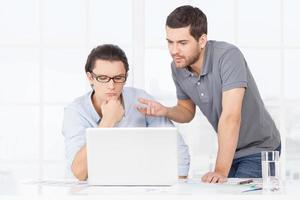 Discussing project. Two confident business people in casual wear discussing something and gesturing while looking at the laptop photo