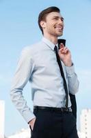 hombre de negocios feliz. apuesto joven en ropa formal sosteniendo su chaqueta en el dedo y mirando hacia otro lado mientras está de pie contra el cielo azul foto