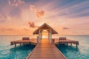 Amazing sunset landscape. Picturesque summer sunset in Maldives. Luxury resort villas seascape with soft led lights under colorful sky. Dream sunset over tropical sea, fantastic nature scenery photo